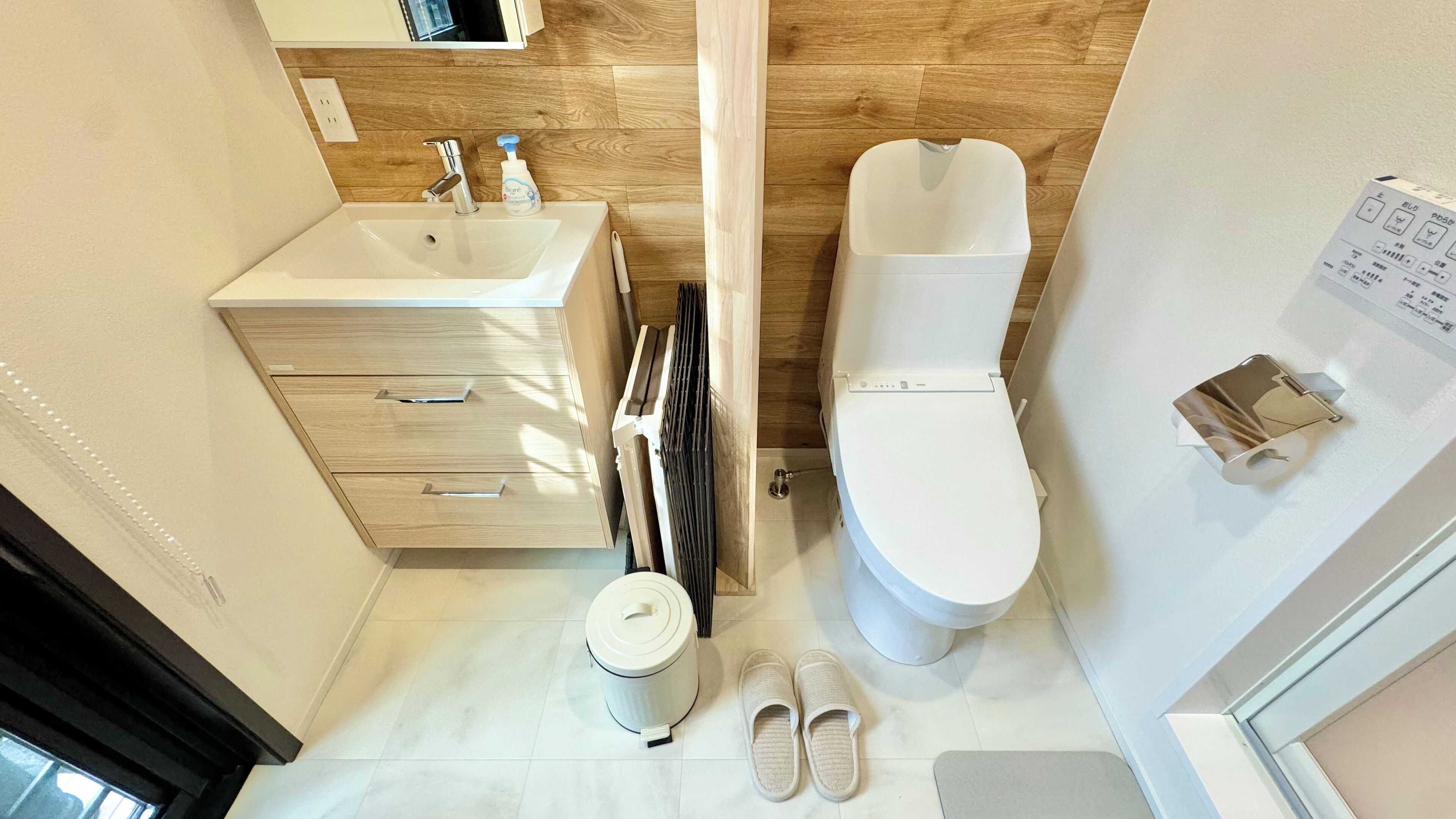 Un baño con un lavamanos blanco, un inodoro y un par de pantuflas en el suelo.