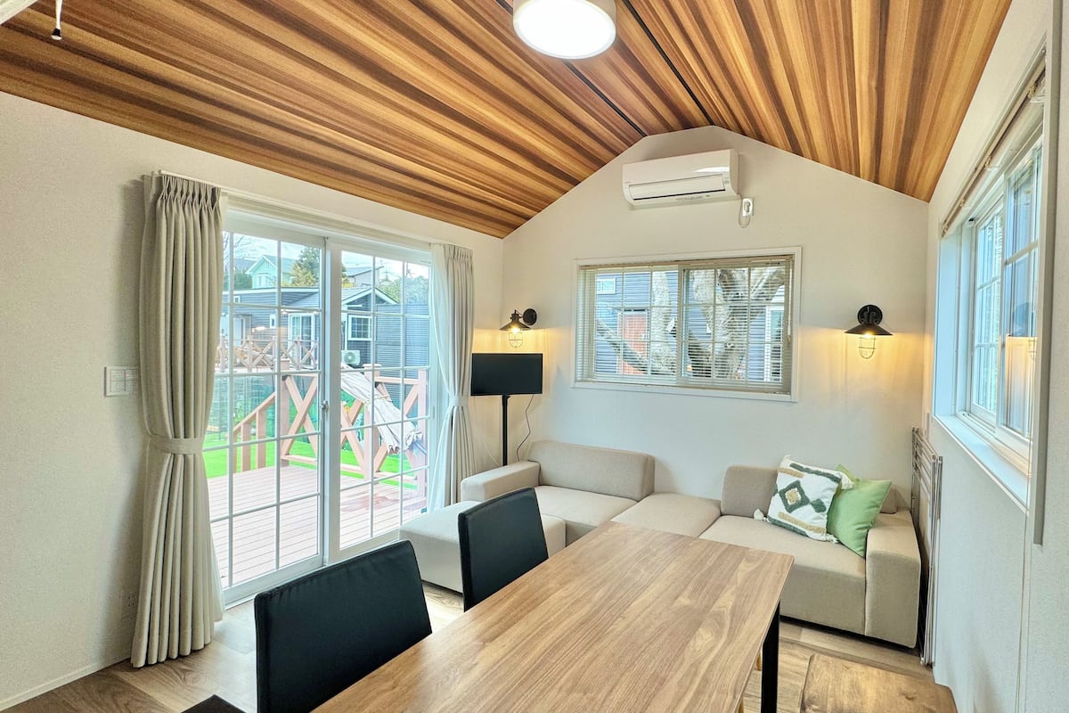 A cozy room with a wooden ceiling, a dining table, a sofa, and two wall-mounted lamps.