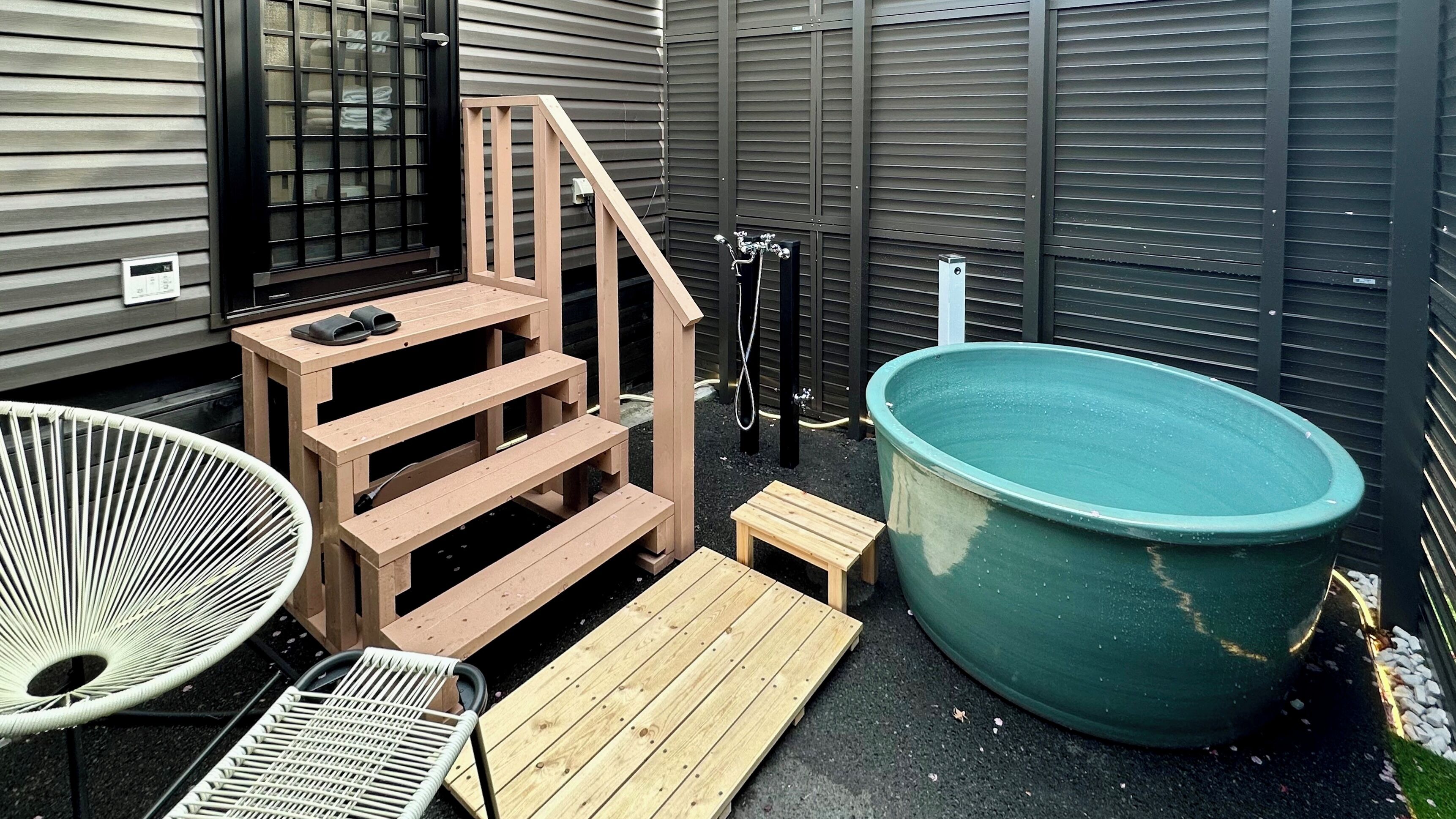 Un patio trasero con una escalera de madera, un jacuzzi, una silla blanca y una pequeña mesa.