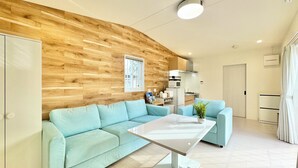 Un salon moderne avec un mur d’accent en bois, un canapé bleu clair, une table basse blanche et un coin cuisine équipé d’un four à micro-ondes et de placards.