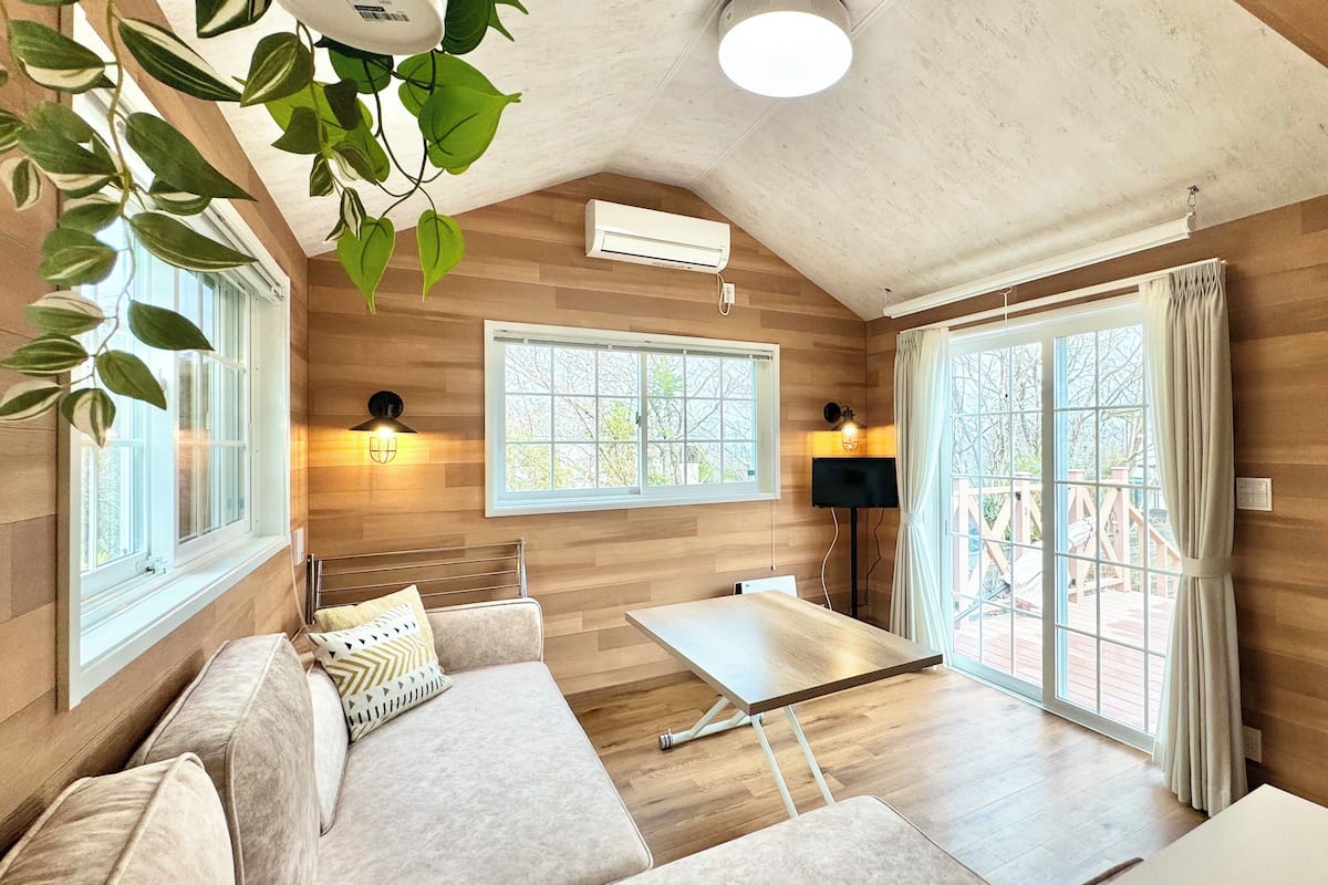 A cozy room with a wooden floor, a sofa, a table, and two windows with curtains.