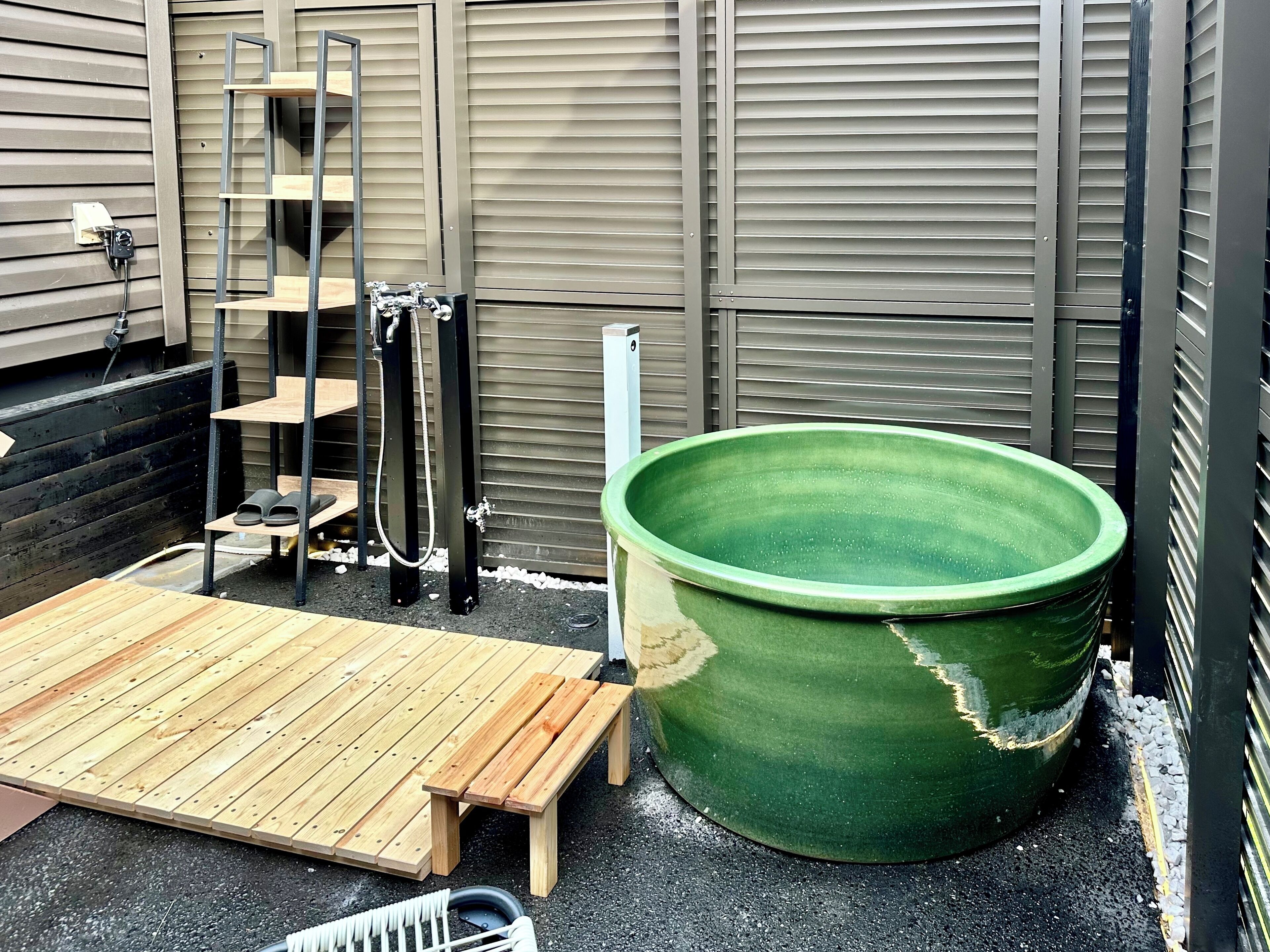 Una terraza de madera con una bañera verde, una escalera y una manguera.