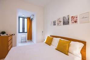 Habitación de hotel con una cama grande, un aparador de madera, una mesita y una ventana con cortinas.