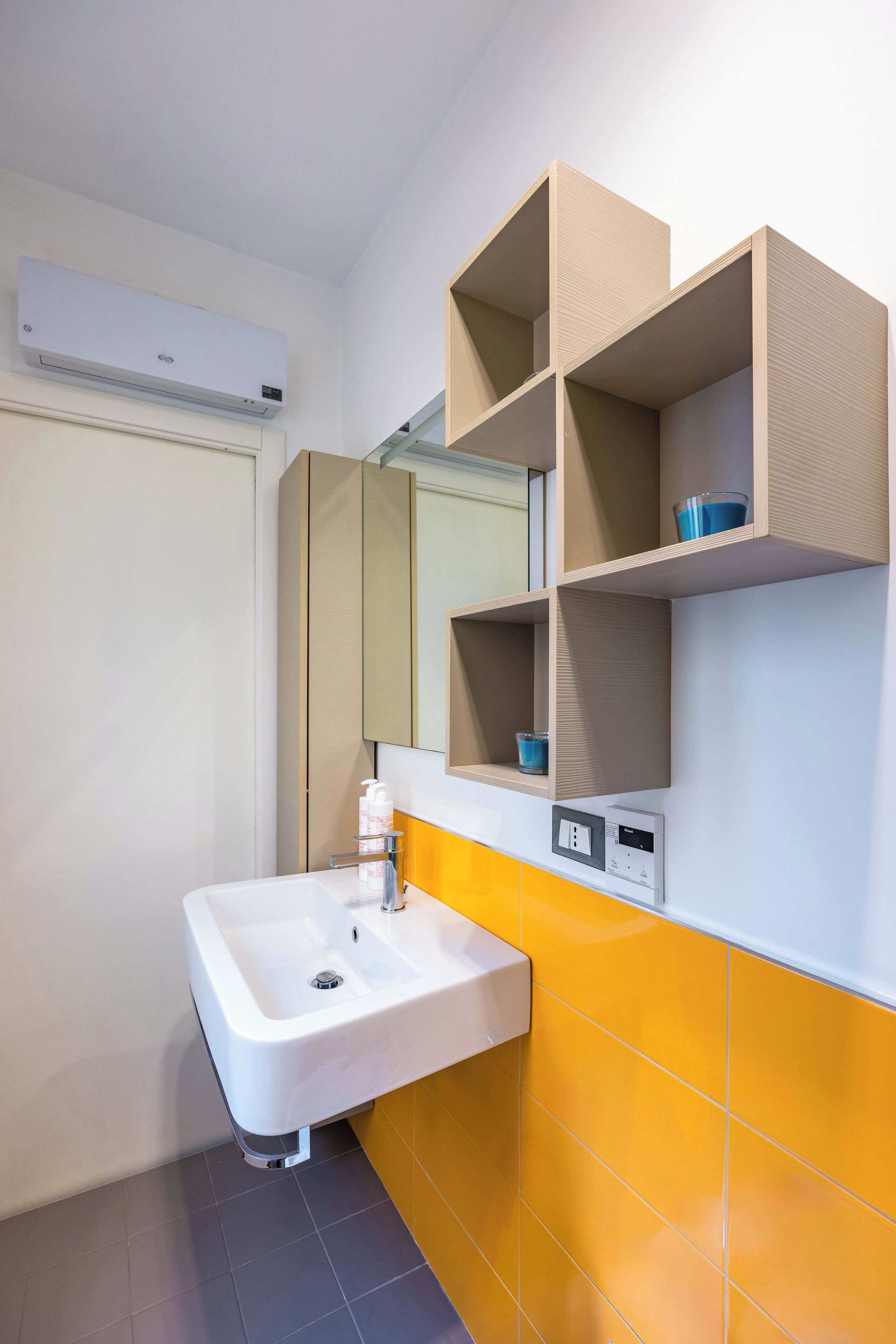 A bathroom with a white sink, yellow tiles, a mirror, and a wall-mounted air conditioner.