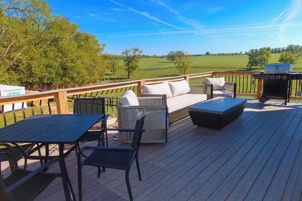 Una terraza con mobiliario exterior, una parrilla y vistas a un campo verde.