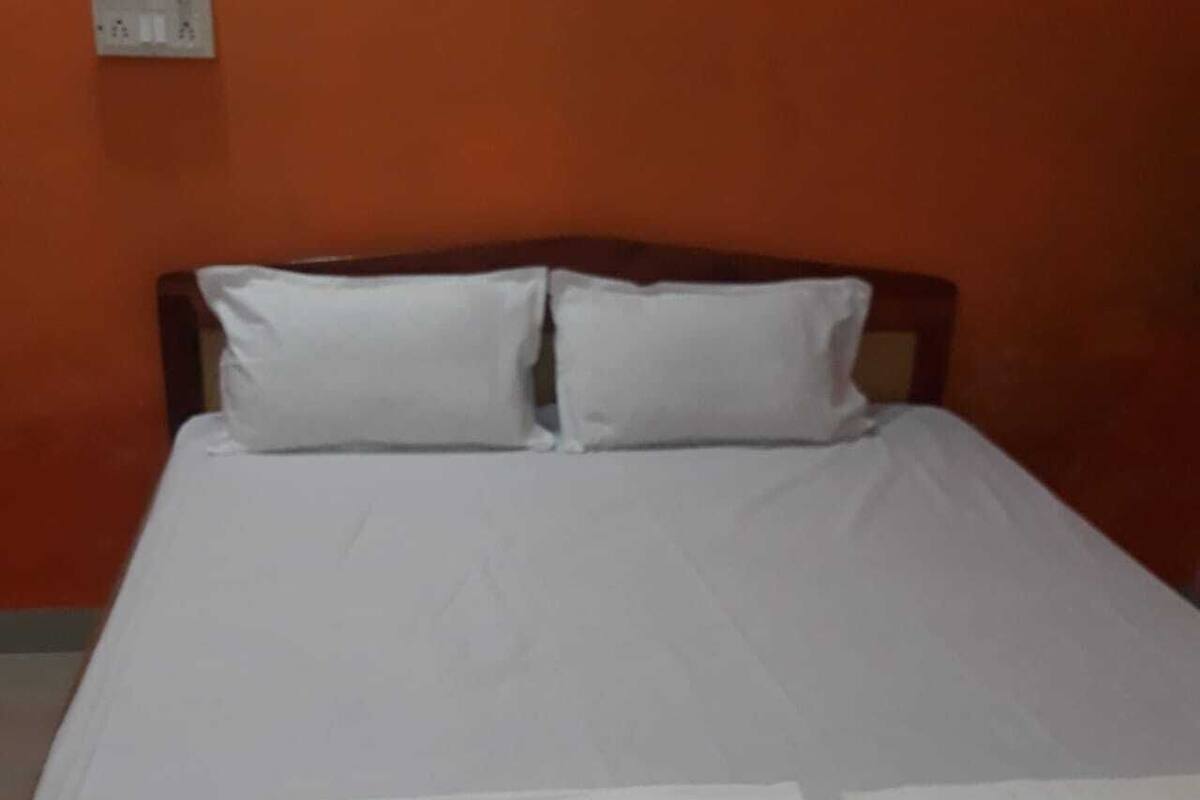 A bed with white bedding and two pillows in a room with orange walls.