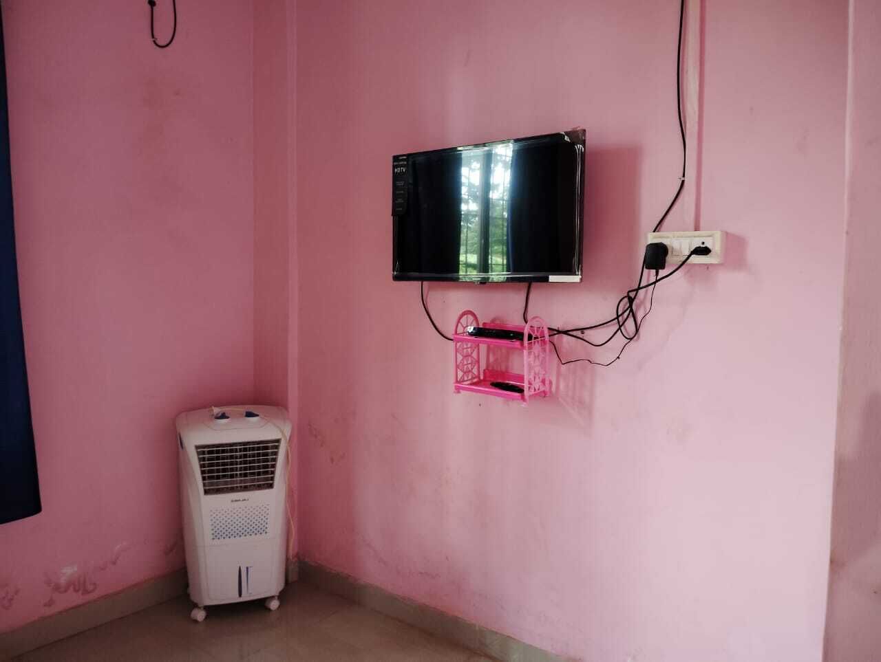 Een kamer met roze wanden, een witte luchtkoeler, een roze tv-meubel en een flatscreen televisie die aan de muur hangt.