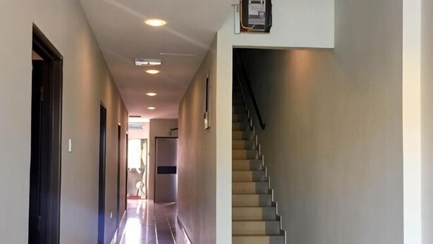 En gang med trappe, en dør til venstre og en lampe på væggen.