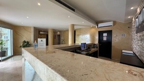 Zona de recepción con mostrador de mármol, mostrador de información, ascensor y equipo de aire acondicionado instalado en la pared.