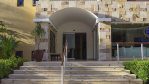 Entrada de hotel con fachada de piedra, una planta grande en maceta y una escalera que lleva a la entrada.