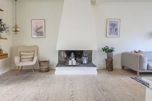 Ein Wohnzimmer mit Kamin, einem Sessel, einer Couch und gerahmten Kunstwerken an den Wänden.