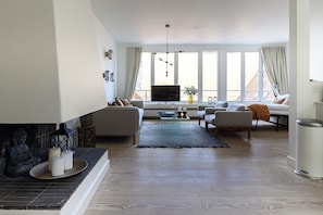 Ein Wohnzimmer mit Kamin, Sofas, einem Fernseher und großen Fenstern.