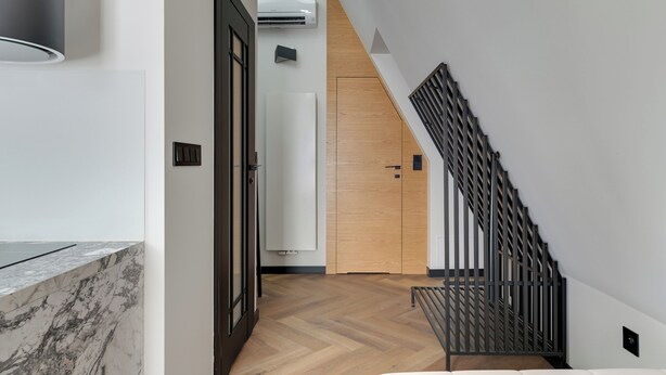 Un interior moderno con piso de madera, una escalera con barandilla de metal y una puerta blanca.