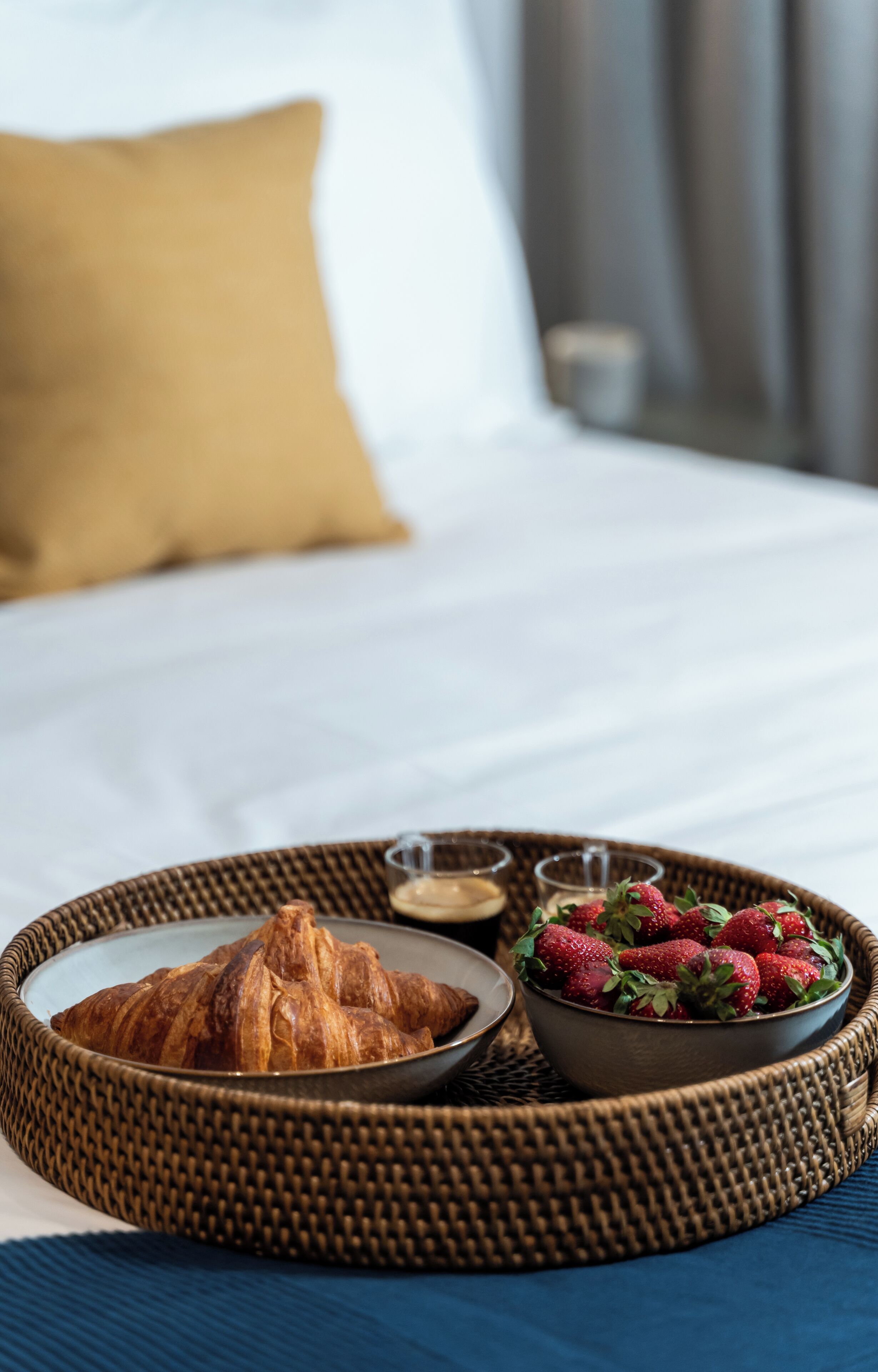 A breakfast tray with croissants and strawberries on a bed with a blue bedspread.