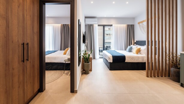 Una habitación de hotel moderna con dos camas, un armario de madera, una planta grande en maceta y vistas a la ciudad.