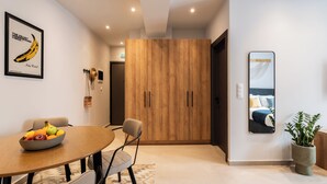 Habitación de hotel moderna con un armario de madera, una zona de comedor con frutero y un espejo grande que refleja la cama.