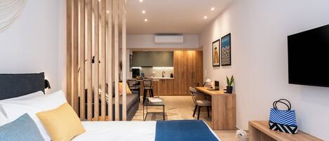 A modern hotel room with a bed, a desk, a chair, and a kitchenette.