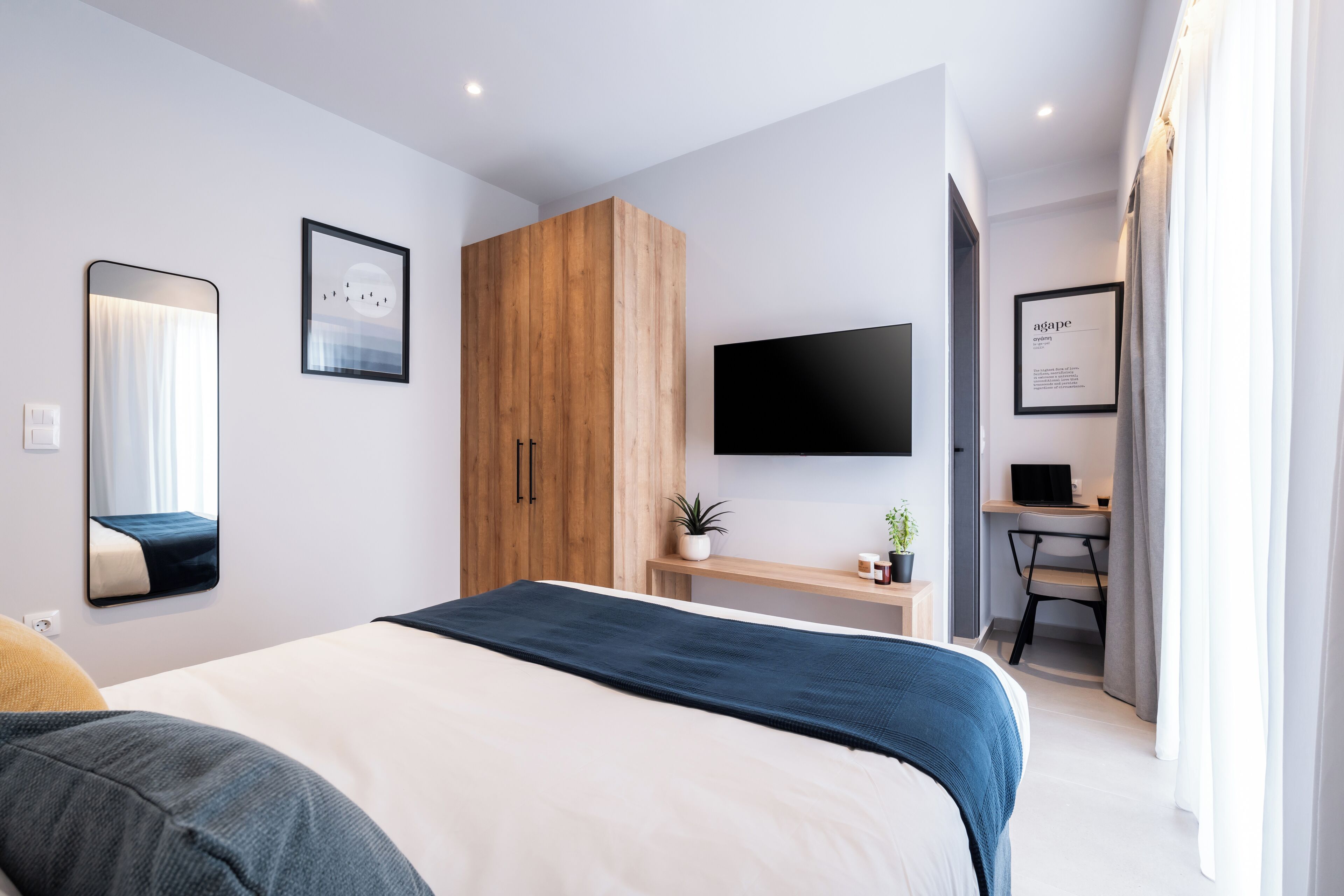 A modern bedroom with a bed, a wardrobe, a desk with a computer, and a TV.