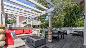 Eine Holzterrasse mit Sitzgelegenheiten im Freien, einer Feuerstelle und einer Pergola.