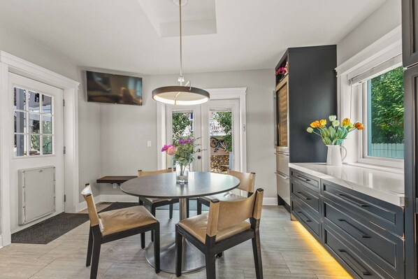 A modern kitchen with a round dining table, dark cabinetry, and a large window with a view of greenery.