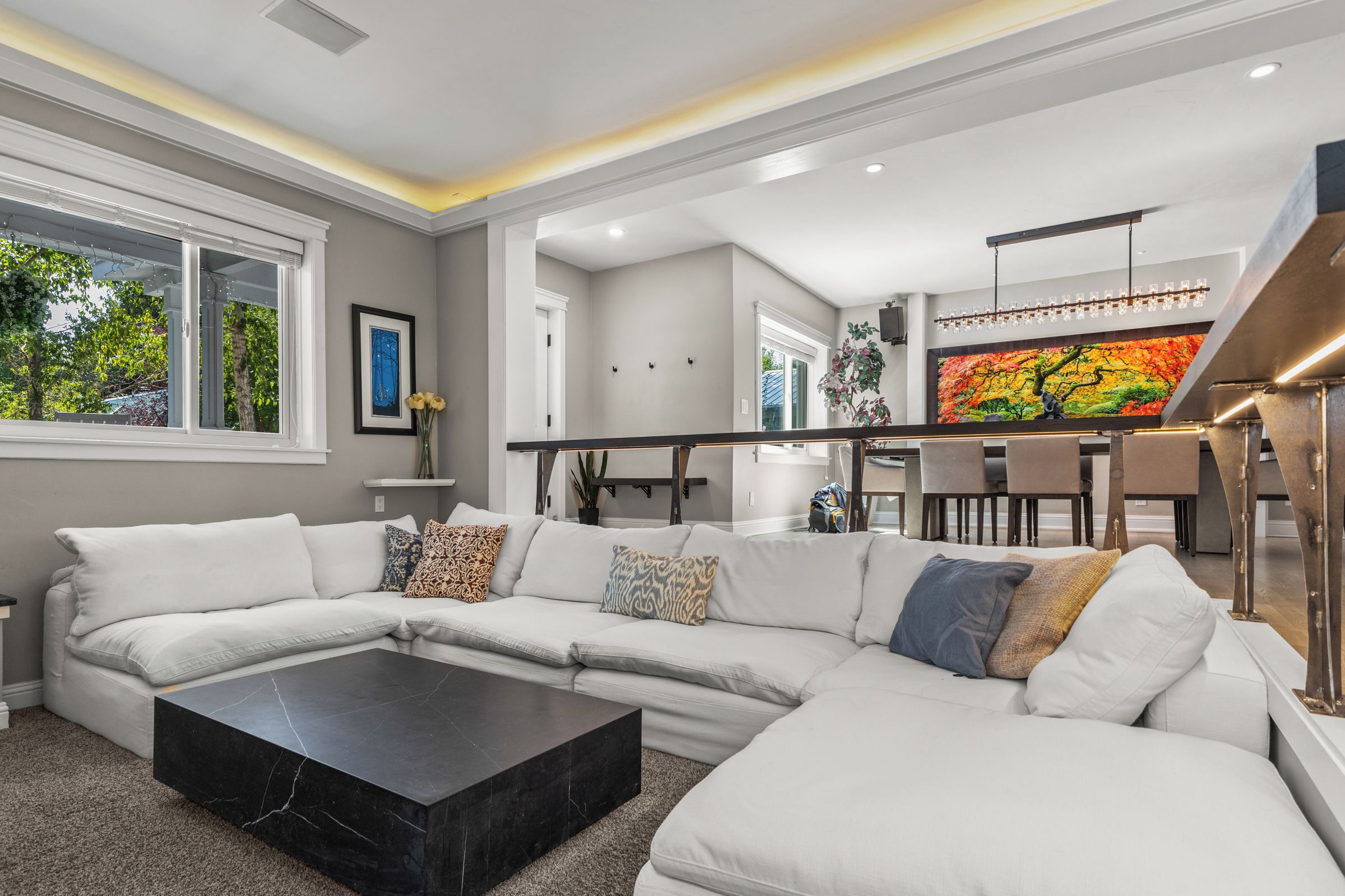 A modern living room with a sectional sofa, a black coffee table, and a dining area with a colorful mural.