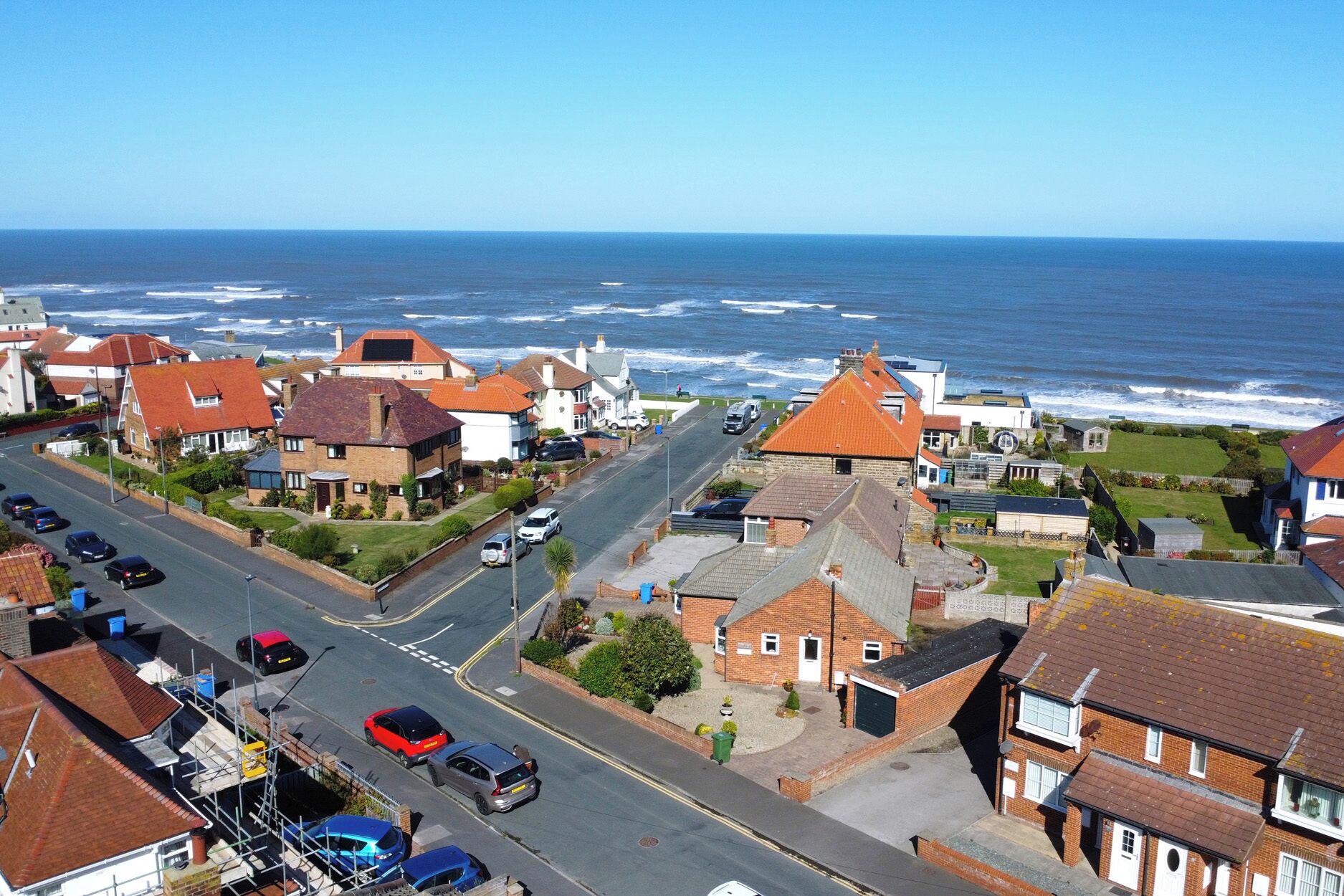 Una zona residencial costera con casas, una carretera y el mar al fondo.