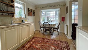 Una cocina con armarios blancos, una mesa de comedor con sillas, un tapete estampado y una ventana con vistas al exterior.