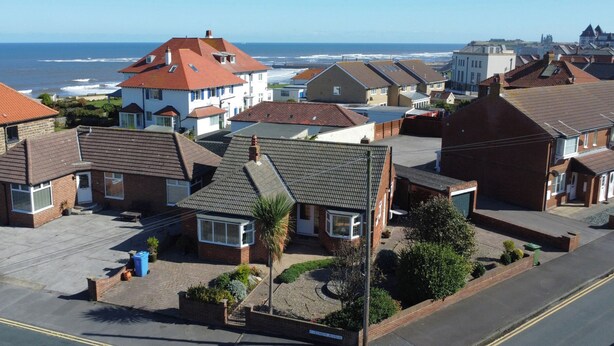 Zona residencial con casas, vista despejada al mar y una calle llamada 'CAEDMON AVENUE'.