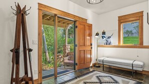 Una habitación con una puerta de madera que da a una puerta de cristal, un banco, una lámpara y un perchero.