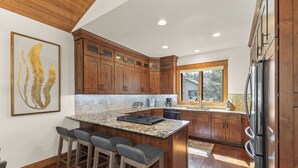 Una cocina con armarios de madera, encimera de granito, una isla integrada con taburetes de bar, refrigerador y una ventana que proporciona luz natural.