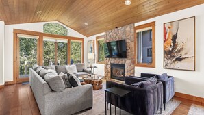 Un salón amplio con chimenea de piedra, ventanas grandes y un televisor moderno.