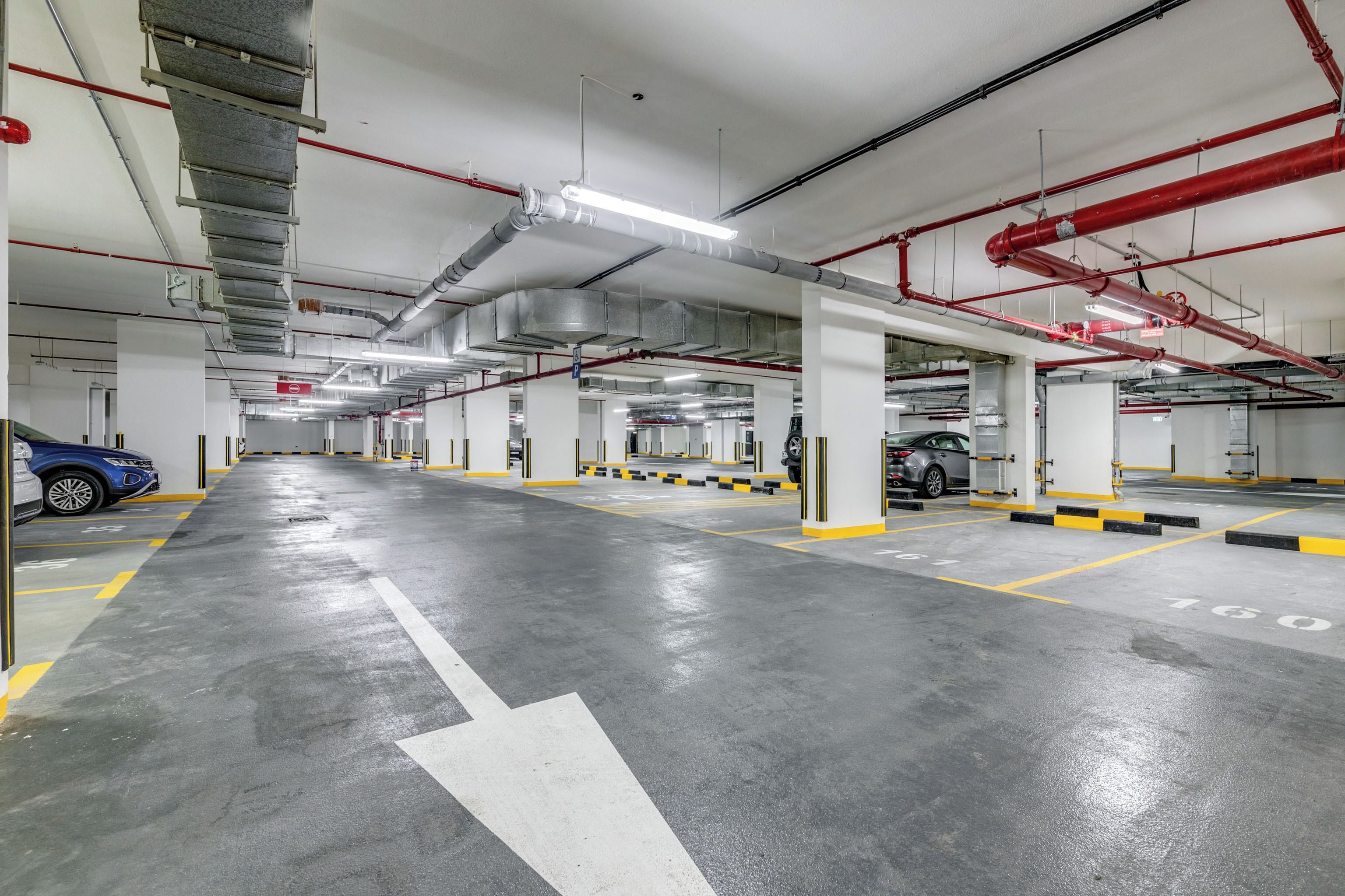 Un parcheggio multipiano con chiare frecce direzionali sul pavimento, colonne strutturali ben visibili e illuminazione superiore.