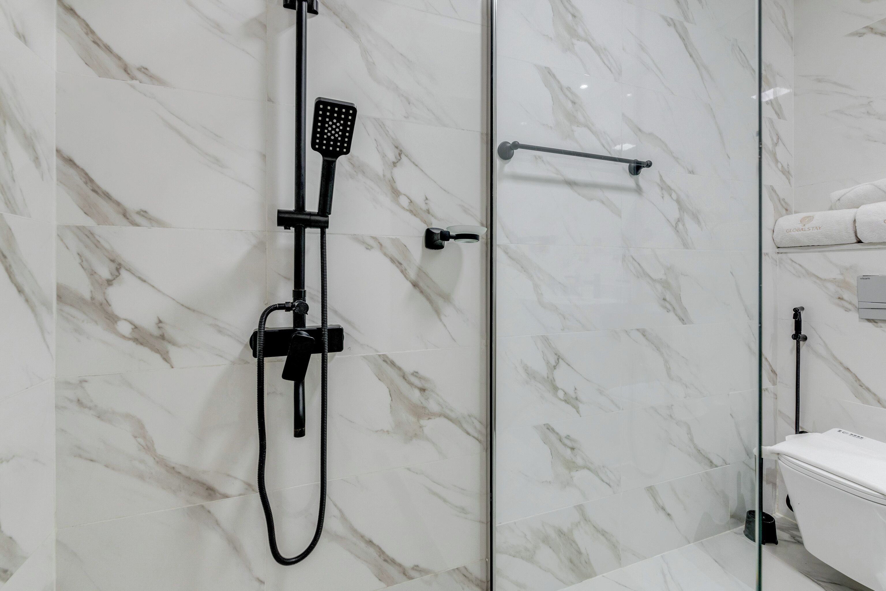 Ein modernes Badezimmer mit einer Glaskabine zur Dusche, weißen Marmorfliesen und einer weißen Toilette.