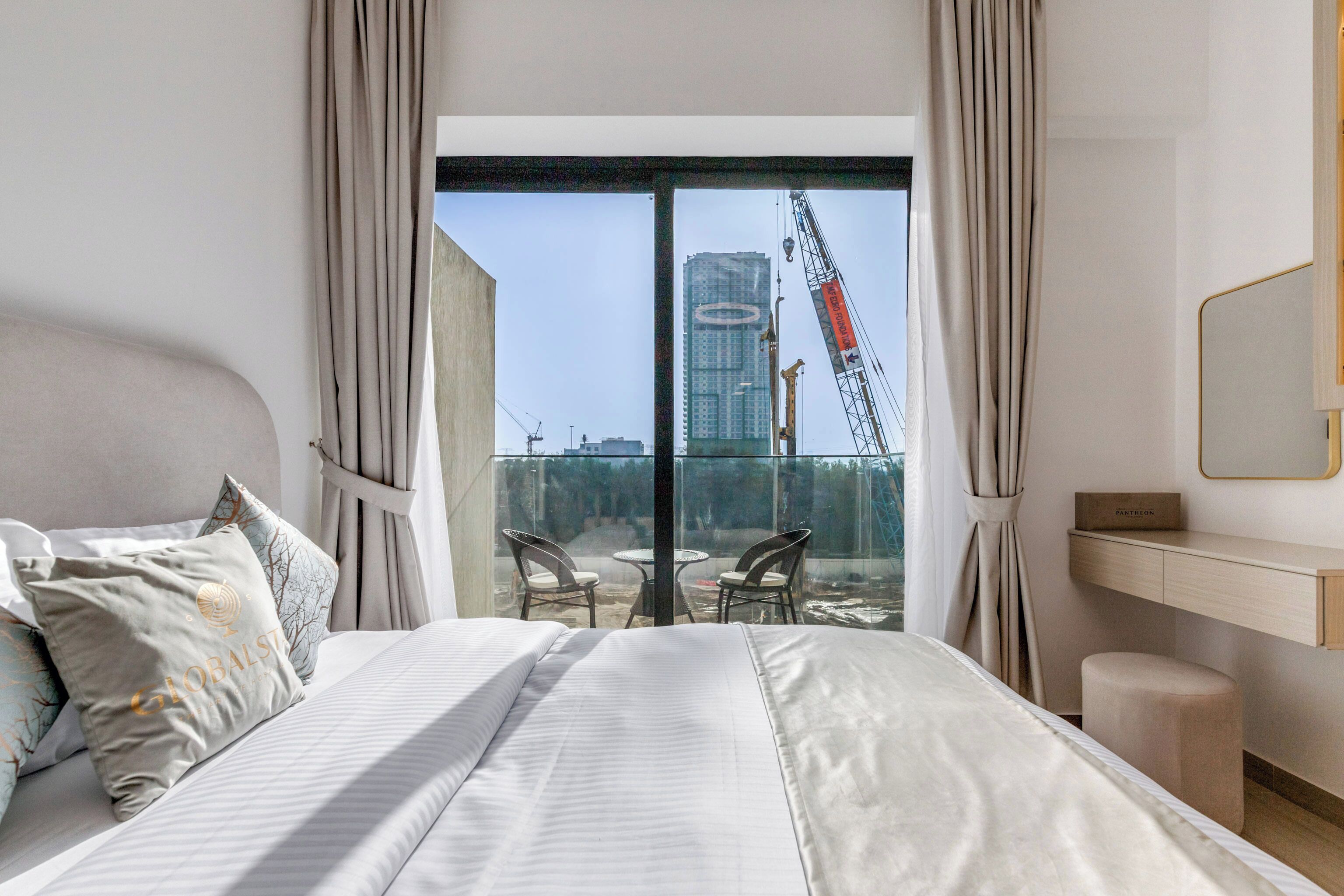 Ein Hotelzimmer mit einem großen Bett, einem Schreibtisch und Blick auf eine Baustelle durch eine Glastür.