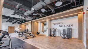 A modern gym with exercise equipment, a wooden floor, and a motivational wall saying "NO PAIN NO GAIN".