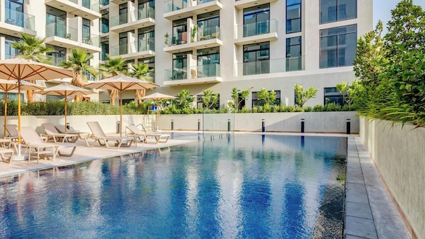 A modern hotel with a swimming pool, sun loungers, and palm trees.