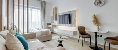 Un salon moderne avec un canapé, une table basse et des fauteuils. Un téléviseur est fixé au mur et un vase décoratif est posé sur une table d’appoint.