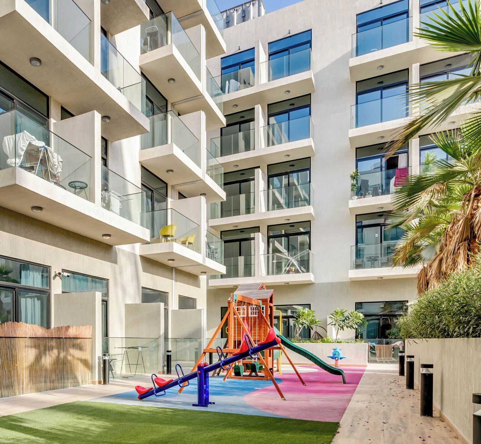 A modern building with multiple balconies, a playground with a slide, and a well-maintained lawn.