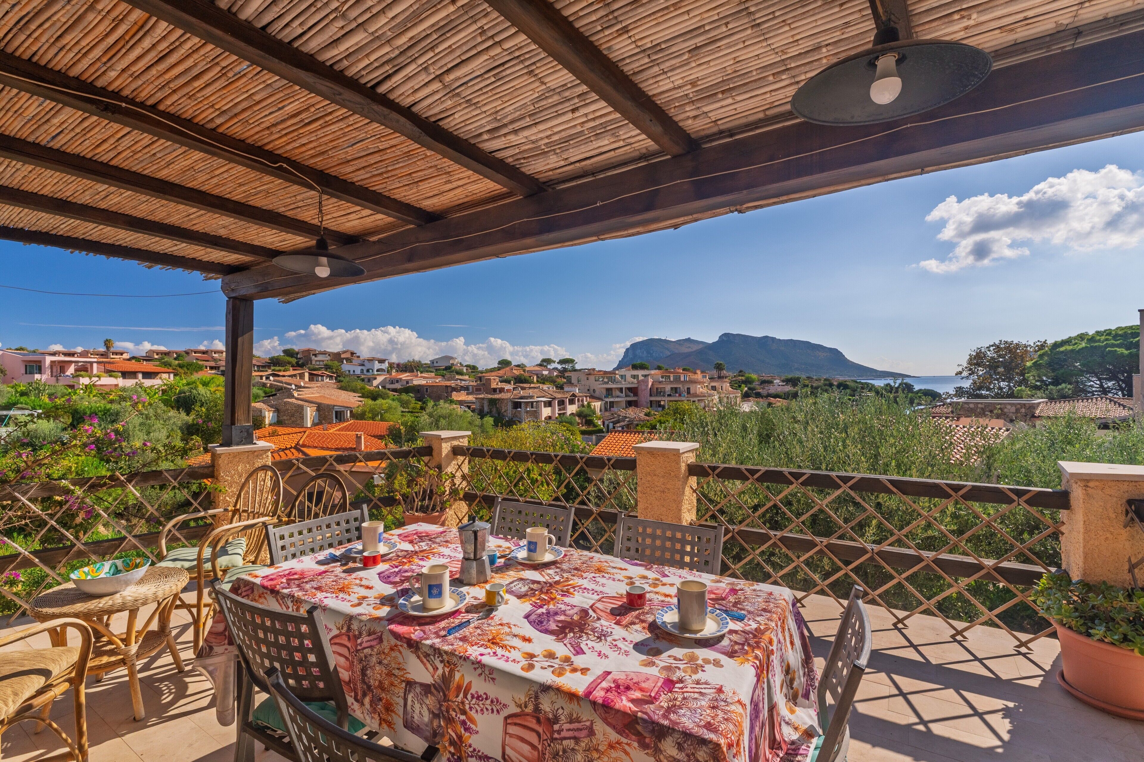 A terrace with a table set for dining, overlooking a scenic landscape with buildings and mountains.