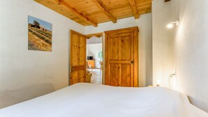 Ein Schlafzimmer mit einem großen Bett, Holztüren, einer Decke mit freiliegenden Balken und einer an der Wand montierten Leuchte.