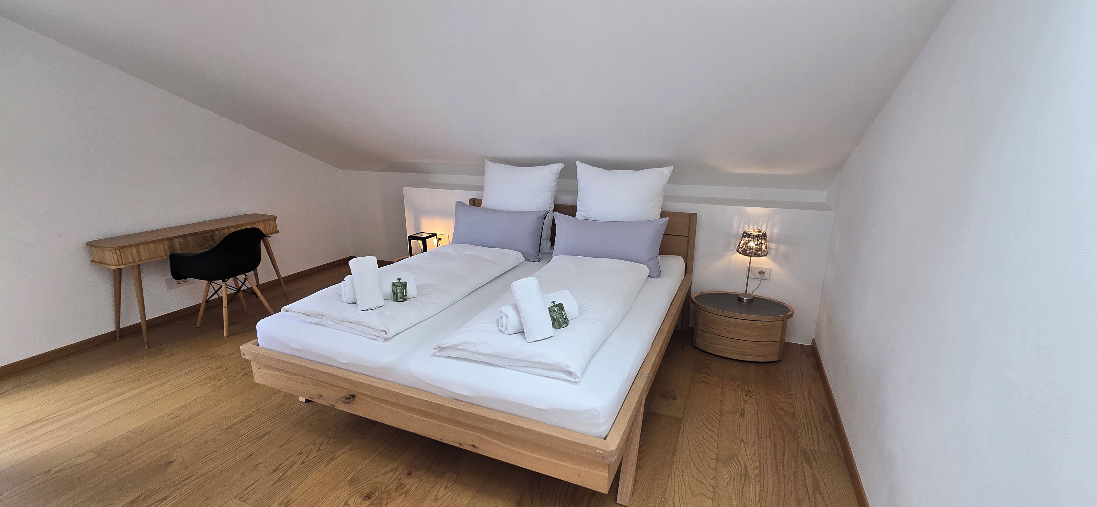 A neatly arranged bedroom with a wooden bed, a desk, and a bedside lamp.