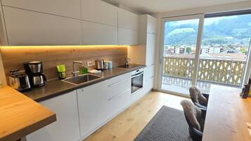 Una cucina moderna con un'ampia finestra, un'area pranzo con tavolo in legno e vista su un paesaggio montuoso.