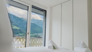Une chambre d’hôtel avec un lit, une fenêtre donnant sur les montagnes et une armoire blanche.