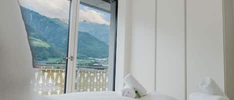 A hotel room with a bed, a window with a mountain view, and a white wardrobe.