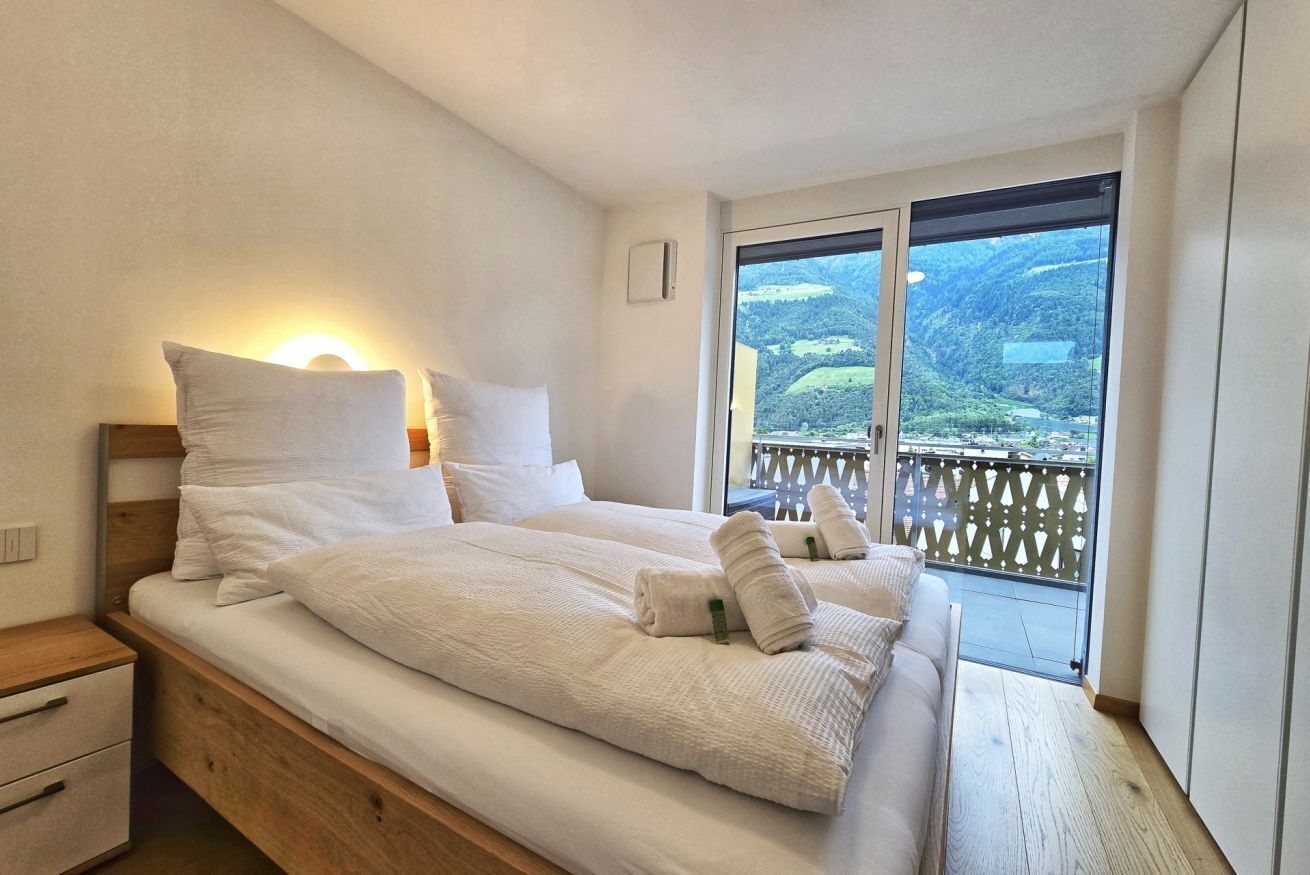 A bedroom with a large bed, a nightstand, and a window with a view of a mountainous landscape.