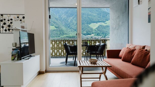 Un salon moderne avec un canapé, un téléviseur et un balcon offrant une vue sur les montagnes.