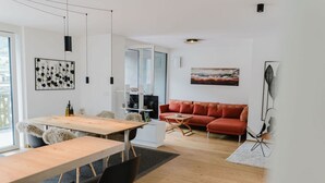Un salon moderne avec une table à manger en bois, des chaises noires, un canapé rouge et une porte en verre donnant sur la cuisine.