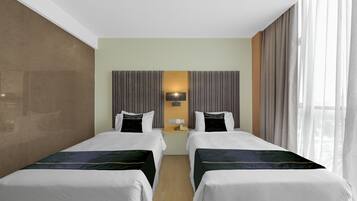 A hotel room with two beds, a nightstand, a lamp, and a large window with curtains.