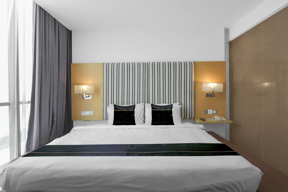 Une chambre d’hôtel avec un grand lit, deux lampes de chevet, une table de chevet avec un téléphone et une vue sur l’extérieur.