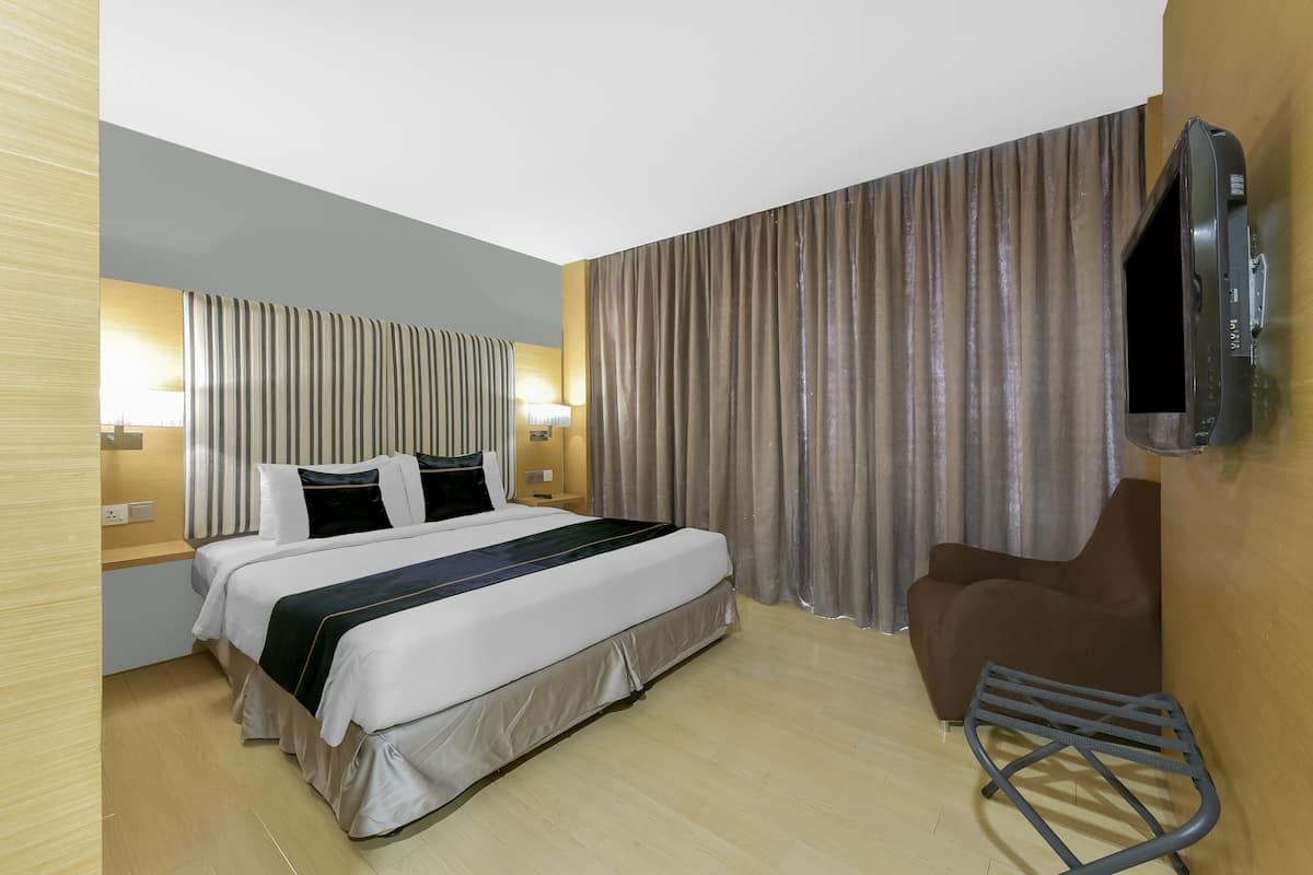 Une chambre d’hôtel avec un lit, un téléviseur fixé au mur, une chaise et des rideaux.